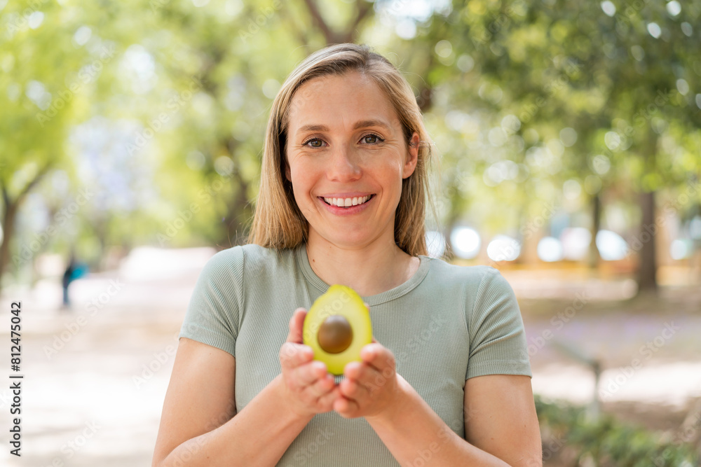 Young blonde woman at outdoors holding an avocado with happy expression Young blonde woman at outdoors holding an avocado with happy expression