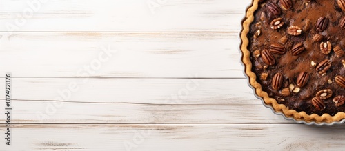 A flat lay photograph of a homemade Chocolate Walnut Derby Pie taken from above on a white wooden surface providing ample copy space