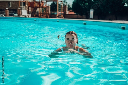 A woman is swimming in a pool. She is smiling and looking at the camera. The pool is blue and the water is calm.