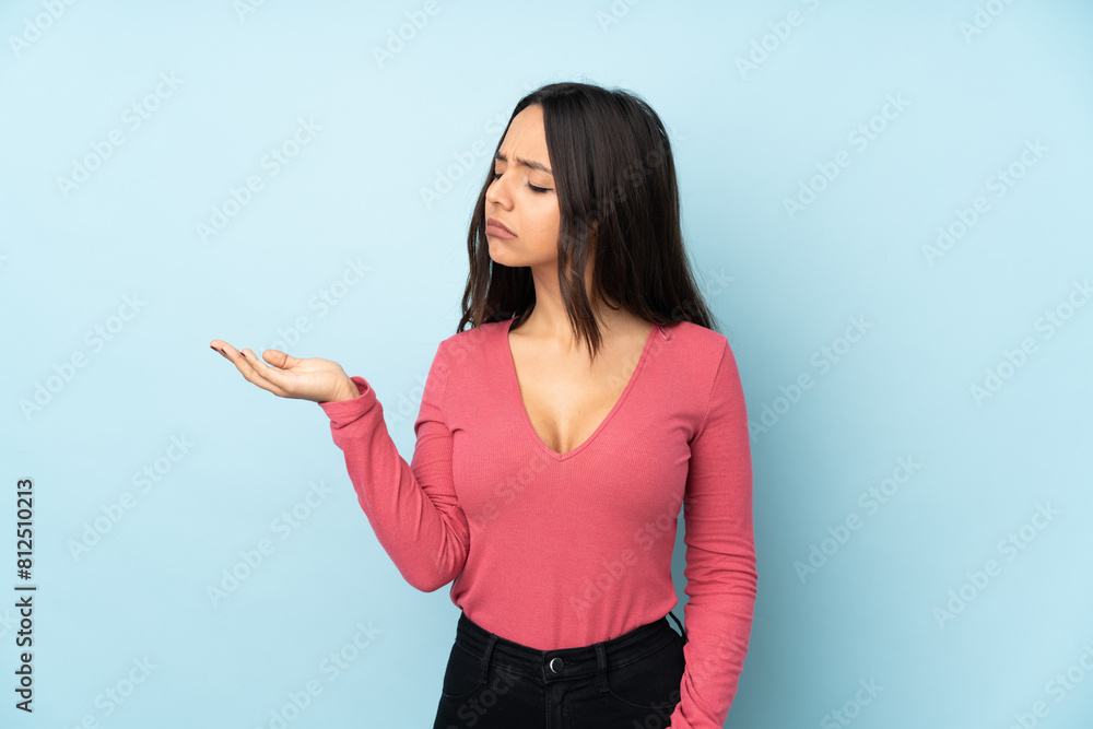 Young mixed race woman isolated on blue background holding copyspace with doubts Young mixed race woman isolated on blue background holding copyspace with doubts