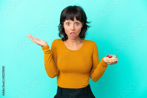 Young mixed race woman holding a tartlet isolated on blue background with shocked facial expression photo