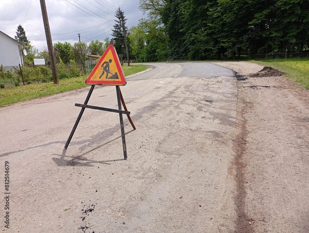 The road works sign stands in the middle of the road and blocks the carriageway. road signs are posted temporarily during road surface repair. The road works sign stands in the middle of the road and blocks the carriageway. road signs are posted temporarily during road surface repair.