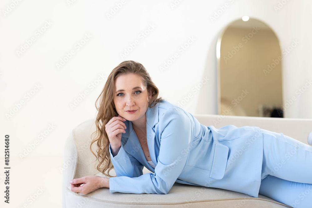 A young attractive woman in a blue suit is lying on a light sofa A young attractive woman in a blue suit is lying on a light sofa