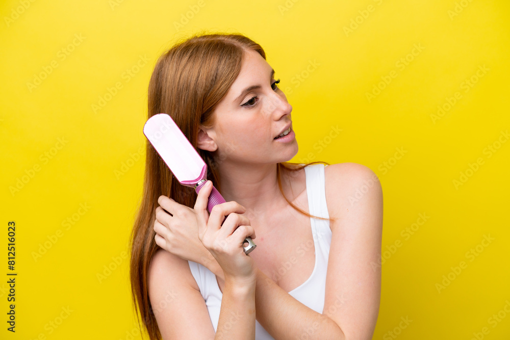 Young redhead woman isolated on yellow background with hair comb Young redhead woman isolated on yellow background with hair comb