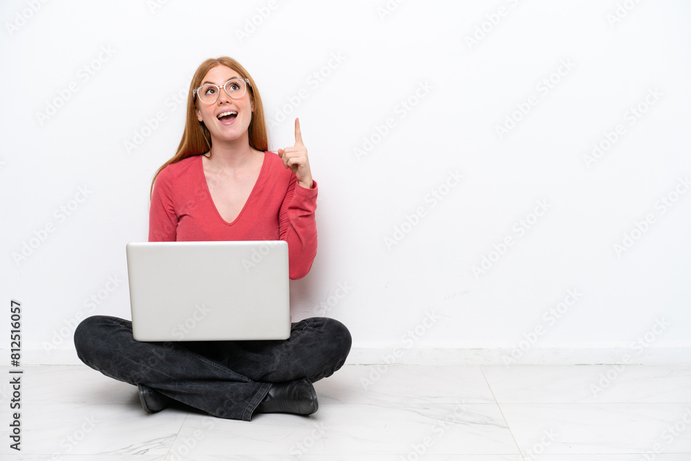 Young redhead woman with a laptop sitting on the floor isolated on white background pointing up and surprised Young redhead woman with a laptop sitting on the floor isolated on white background pointing up and surprised