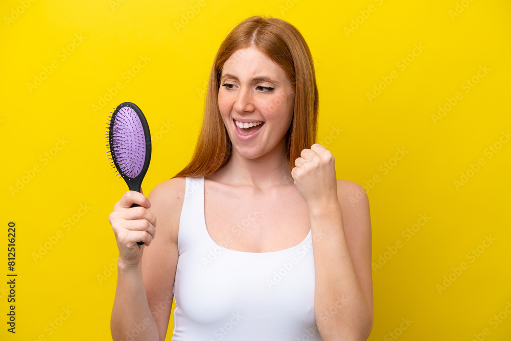 Young redhead woman holding a hairbrush isolated on white background celebrating a victory Young redhead woman holding a hairbrush isolated on white background celebrating a victory