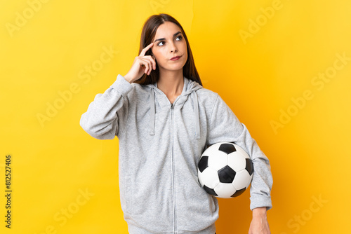 Young football player woman isolated on yellow background having doubts and thinking