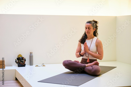 A woman is sitting on a mat and doing yoga prayer position. She is in a relaxed and focused mood.