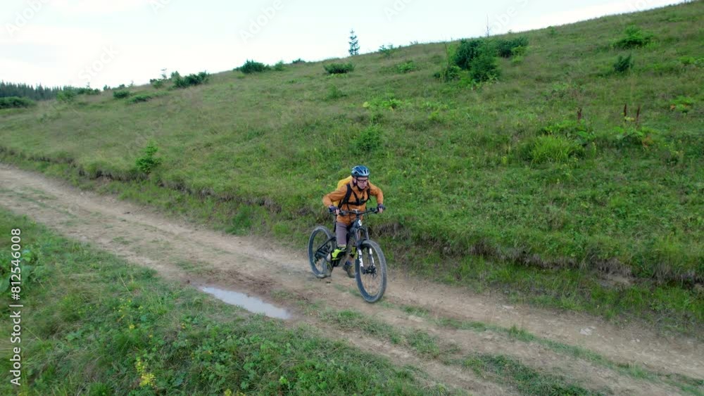 Cyclist man riding electric mountain bike outdoors. Aerial view of male tourist biking along grassy trail in the mountains, wearing helmet and backpack. Concept of sport, active leisure and nature. Cyclist man riding electric mountain bike outdoors. Aerial view of male tourist biking along grassy trail in the mountains, wearing helmet and backpack. Concept of sport, active leisure and nature.