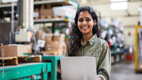 A woman in a green shirt smiling while holding a laptop in a warehouse setting.