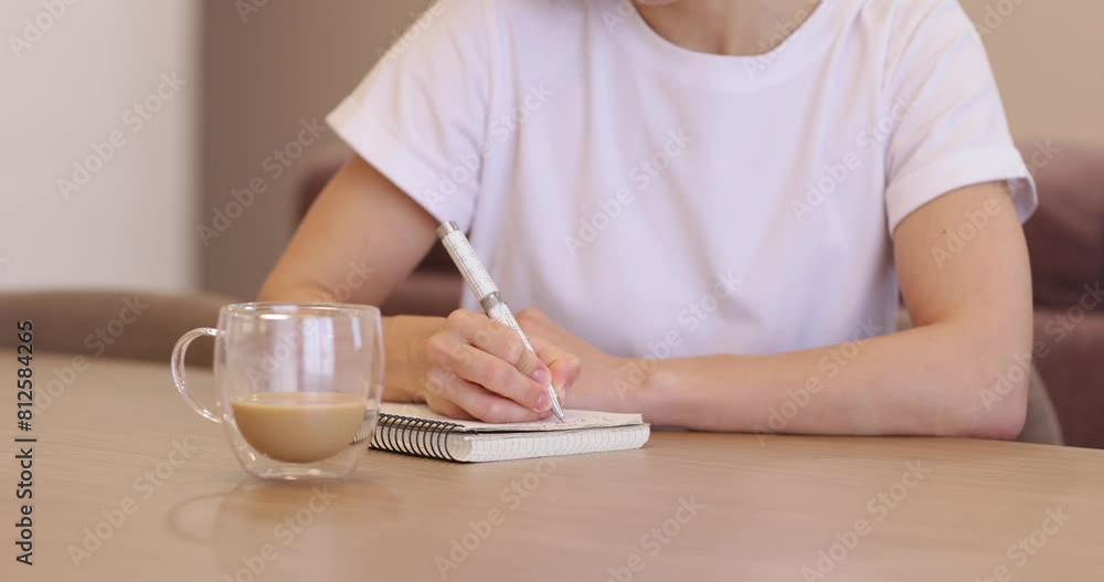 young woman writing down in white notebook and drinking coffee at home young woman writing down in white notebook and drinking coffee at home