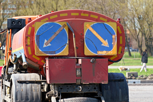 A red and orange truck with two blue signs on the back. The vehicle has large tires with deep tread, perfect for navigating rough terrain and asphalt roads © Маргарита Трушина