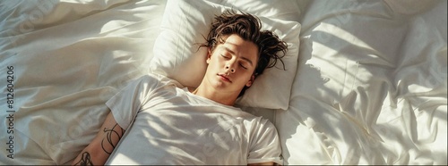 Man is wearing white tshirt sleeping in bed, top view, he is wrapped up under the covers, sunlight shining through the window on to him and making his hair black. photo