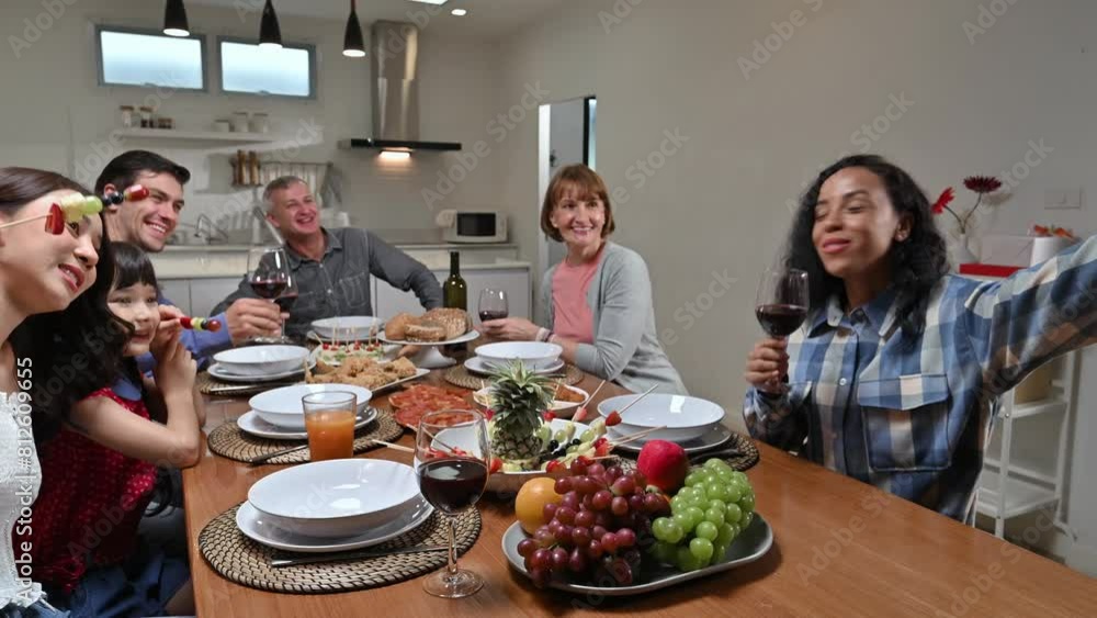 Big family with multi ethnic making selfie video call via mobile phone while eating together christmas party at home. Group of kinfolk various ages celebrating new year party in dining room. Big family with multi ethnic making selfie video call via mobile phone while eating together christmas party at home. Group of kinfolk various ages celebrating new year party in dining room.