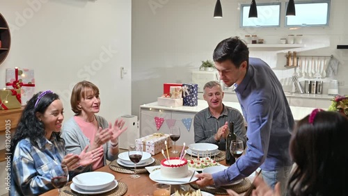Happy little girl celebrating birthday with big family at home. Caucasian father holding a cake surprise daughter while grandparent and mother sing song clap a hand in birthday party in dining room. photo