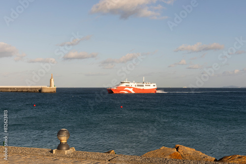 Ferry boat crossing Strait of Gibraltar in Tarifa harbor next to sacred heart of Jesus statue on a bright sunny day