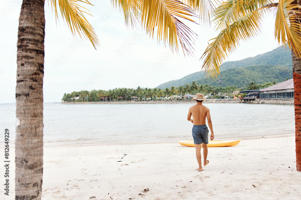Happy Asian Man Kayaking on a Tropical Beach with a Colorful Canoe: Active Leisure and Enjoyment on a Sunny Summer Vacation Happy Asian Man Kayaking on a Tropical Beach with a Colorful Canoe: Active Leisure and Enjoyment on a Sunny Summer Vacation
