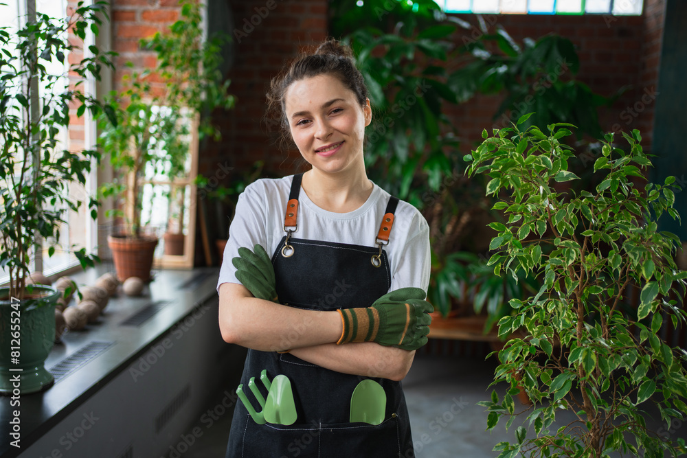 Running of own business. Young woman florist wearing apron in botanical store with green plants. Happy small business owner working at flower shop standing surrounded by plants. Small business Running of own business. Young woman florist wearing apron in botanical store with green plants. Happy small business owner working at flower shop standing surrounded by plants. Small business