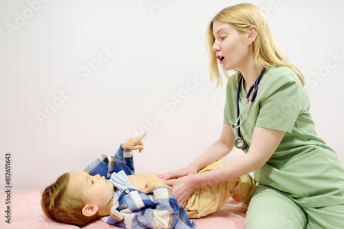 Cute toddler boy is at an appointment with pediatrician. Doctor gastroenterologist palpating belly of little child patient lying on couch in medical office. Gastroenterological diseases of kids