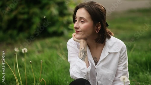 Beautiful young caucasian woman sitting on grass and looking around outdoors Smiling relaxed brunette girl enjoying beautiful day at park Happy people concept