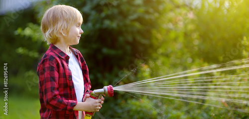 Cute boy watering plants and playing with garden hose with sprinkler in sunny backyard. Preschooler child having fun with spray of water. Summer outdoors activity for kids. Gardening. Banner.