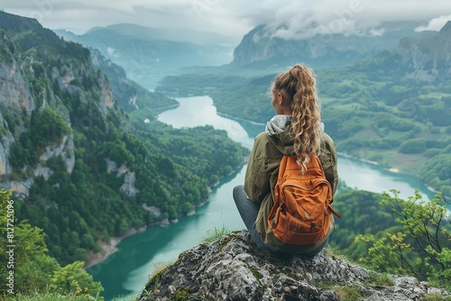 A woman sits atop a mountain, gazing at a lake below