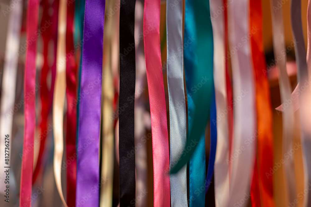 Variety of brightly coloured ribbons, hanging in dappled sunlight. Close up background texture, abstract design element.