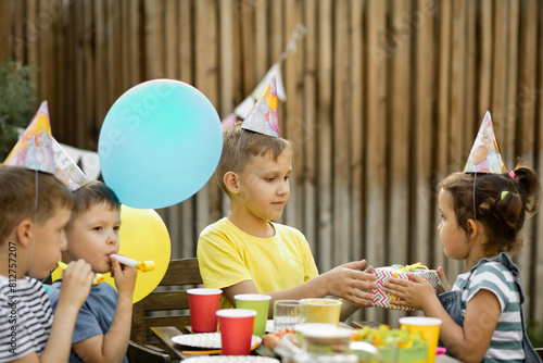 Cute funny nine year old boy celebrating his birthday with family or friends with homemade baked cake in a backyard. Birthday party for kids. His gets presents gift box.