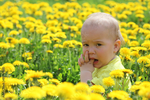 Little cute boy in yellow clothes among dandelions.