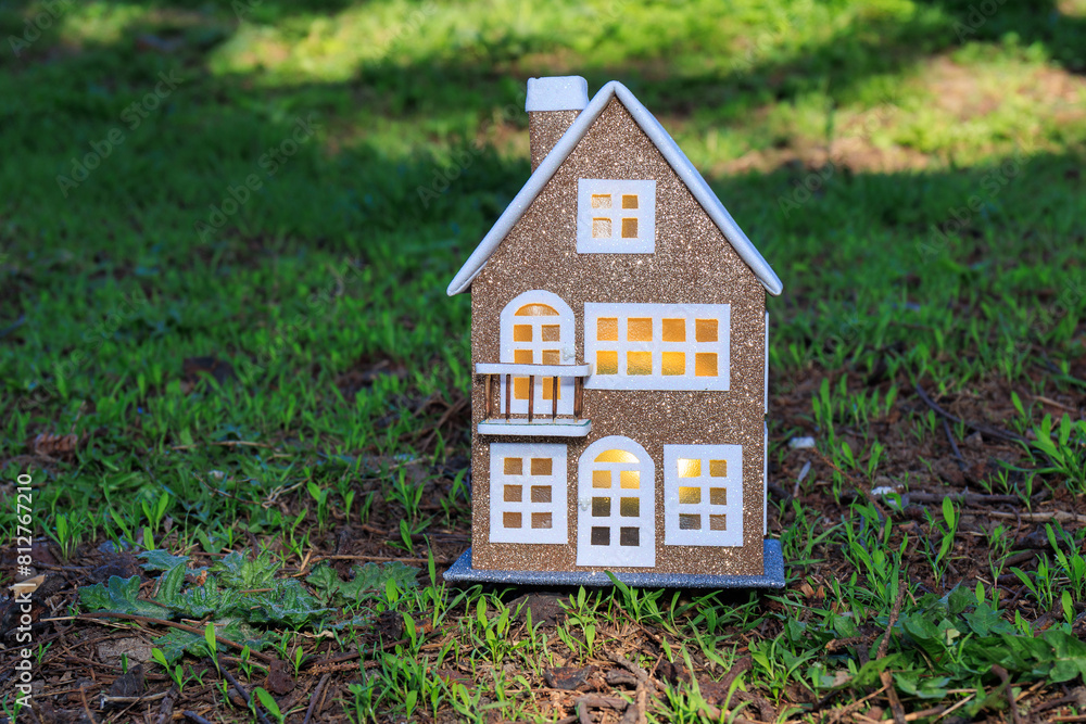 Close-up of a brown house with yellow light in the windows on a semi-blurred background of green grass Close-up of a brown house with yellow light in the windows on a semi-blurred background of green grass