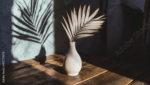 a minimalist interior design featuring a white vase and palm leaf on a wooden table illuminated by shadows from a window high quality photo photo