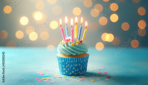 A single cupcake in a blue polka dot wrapper, topped with colorful lit birthday candles photo