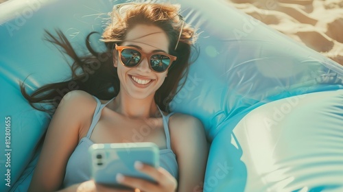 Portrait of charming smiling woman in sunglasses using cellphone and write messages to friends while lying on inflatable mattress on summer beach : Generative AI photo