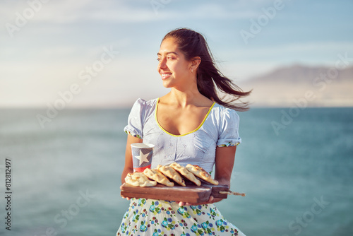 portrait latin woman dressed in typical huasa costume holding pine empanadas and a recyclable cup with flag of Chile outdoors