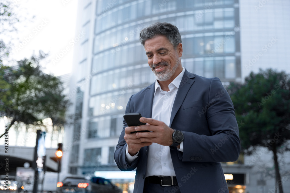 Smiling mature hispanic senior business man using app, holding smartphone cellphone at office centre at night. Indian or latin middle age male entrepreneur businessman working on mobile cell phone. Smiling mature hispanic senior business man using app, holding smartphone cellphone at office centre at night. Indian or latin middle age male entrepreneur businessman working on mobile cell phone.