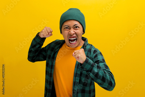 Young Asian man, wearing a beanie hat and casual outfit, is displaying aggression with a defensive gesture, clenched fists, an angry expression, and a readiness to fight, indicating potential anger photo