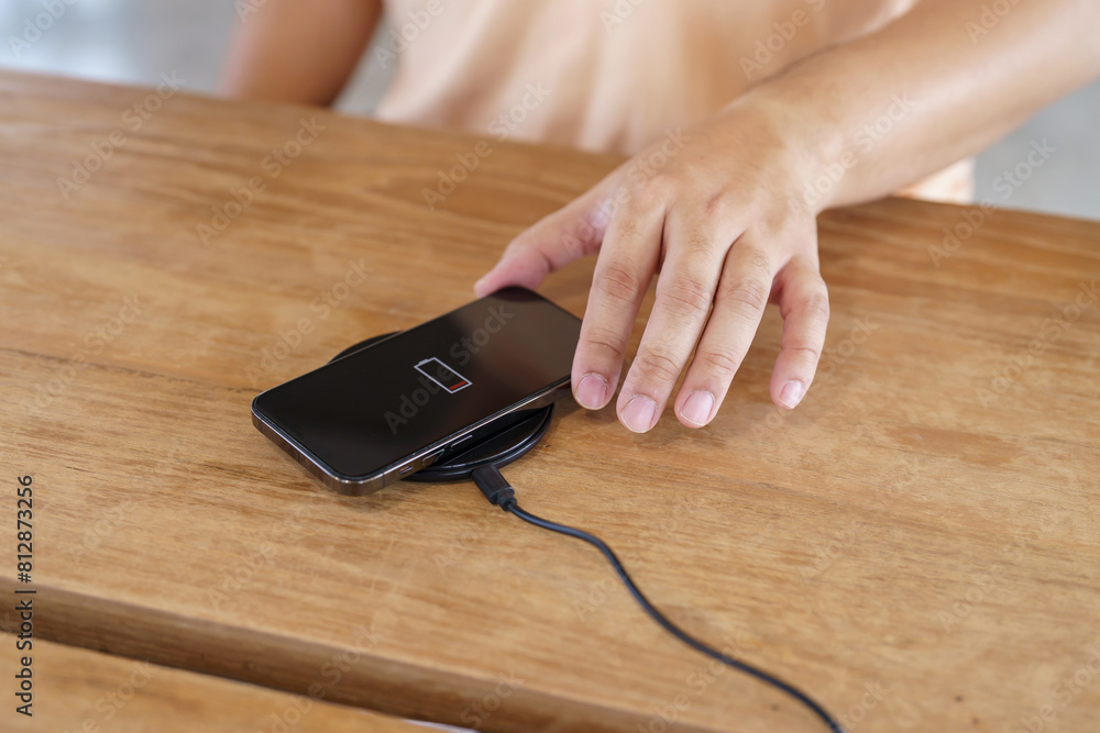 Charging mobile phone battery with wireless charging device in the table. Smartphone charging on a charging pad. Mobile phone near wireless charger Modern lifestyle technology concept. Charging mobile phone battery with wireless charging device in the table. Smartphone charging on a charging pad. Mobile phone near wireless charger Modern lifestyle technology concept.