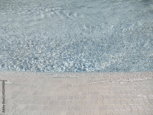 Close-up view of rippling water surface in pool with stone tiles border under sunlight. © Tam
