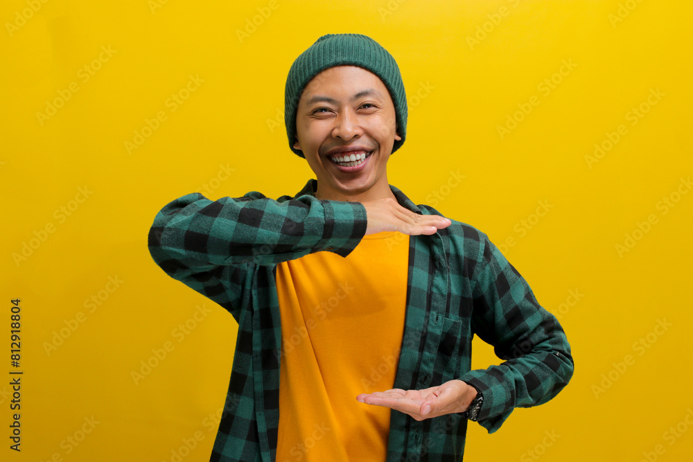 A young Asian man, dressed in casual clothes and wearing a beanie hat, is using hand gestures to indicate a big or large size while smiling at the camera, conveying the concept of measurement or size A young Asian man, dressed in casual clothes and wearing a beanie hat, is using hand gestures to indicate a big or large size while smiling at the camera, conveying the concept of measurement or size