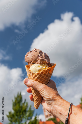 Eistüte mit Eiskugeln in der Hand vor blauem Himmel