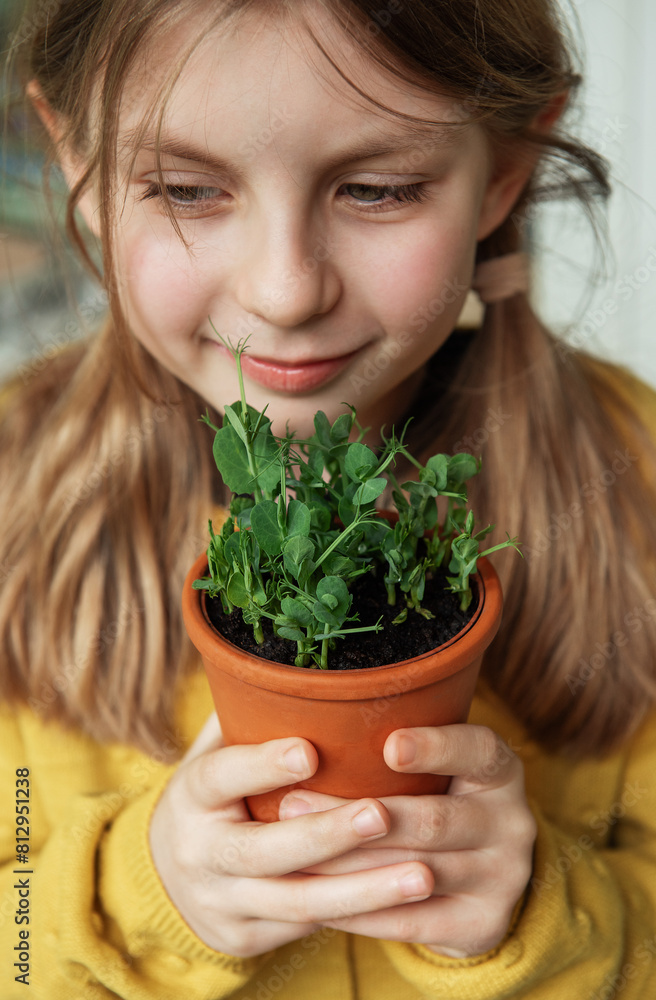 A child, dressed in a vibrant yellow sweater, delicately holds a terracotta pot with a green plant. A child, dressed in a vibrant yellow sweater, delicately holds a terracotta pot with a green plant.