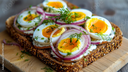 Close-up image showcasing a delicious open-faced sandwich topped with sliced boiled eggs, red onion rings, and fresh dill on whole grain bread