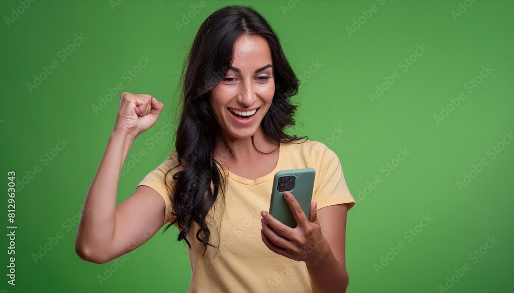 young woman hold in hand use mobile cell phone doing winner gesture on green background young woman hold in hand use mobile cell phone doing winner gesture on green background