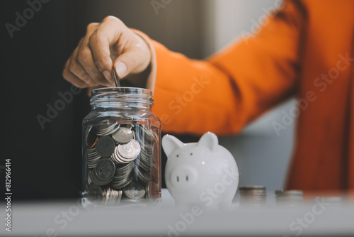 Quadro su tela Beautiful Asian businesswoman insert coins in a pin piggy bank on the table