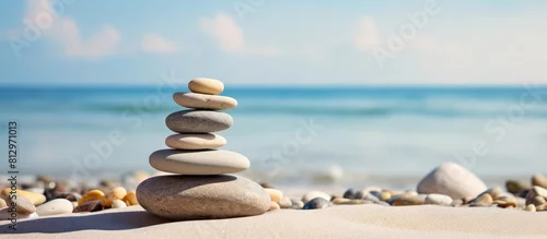 Obraz  z motywem A zen symbol in the form of a pyramid of stones resting on sandy ground representing harmony and balance The image also includes the serene backdrop of the ocean with a closeup of a tower of sea pebb