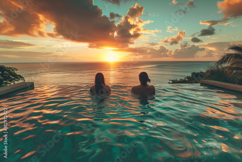Guests lounging in a tranquil infinity pool overlooking the shimmering turquoise ocean at sunset.