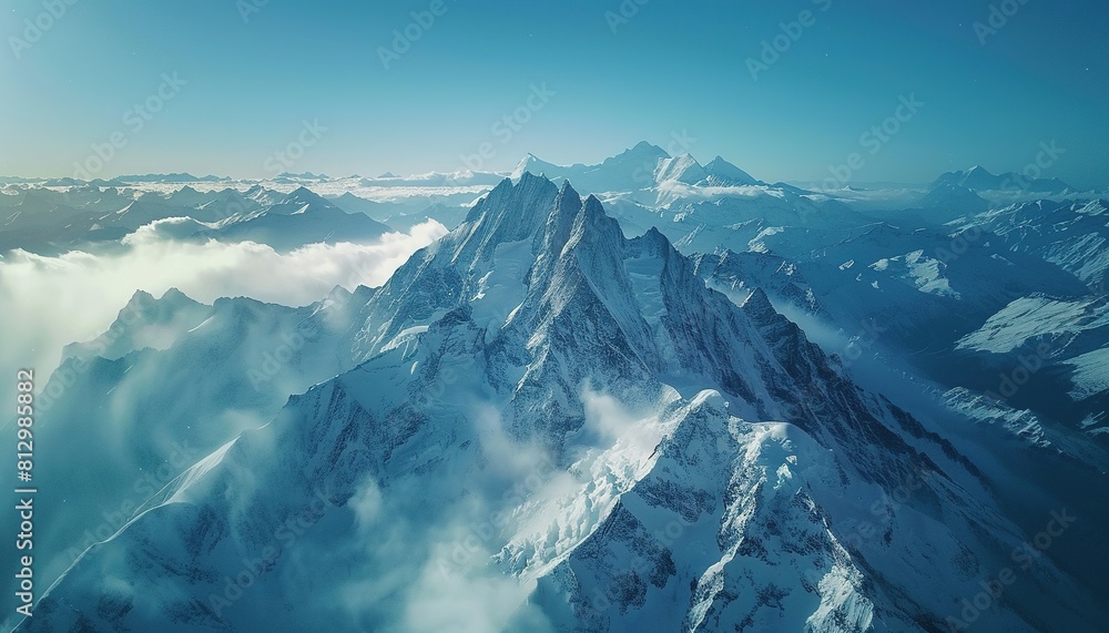 Aerial view of snowcapped mountains in the Alps, with misty peaks and a blue sky Aerial view of snowcapped mountains in the Alps, with misty peaks and a blue sky