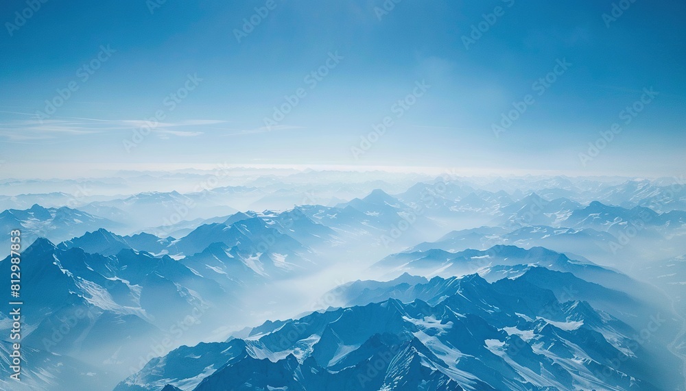 Aerial view of snowcapped mountains in the Alps, with misty peaks and a blue sky