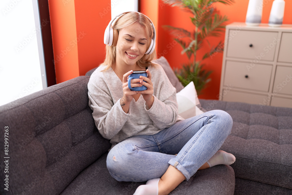 Young blonde woman listening to music drinking coffee at home