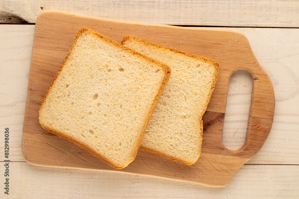 Two pieces of white bread for toaster with wooden kitchen board on wooden table, macro, top view. Two pieces of white bread for toaster with wooden kitchen board on wooden table, macro, top view.